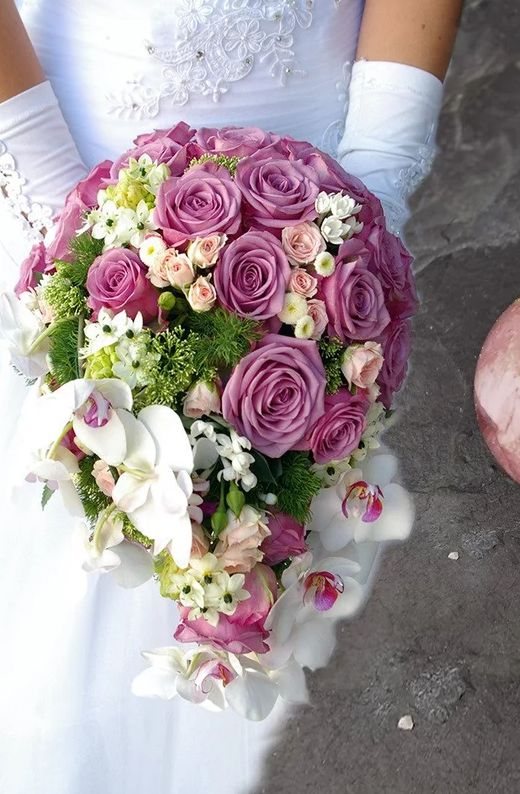 Braut im weißen Kleid mit einem Strauß aus lila Rosen und weißen Orchideen
