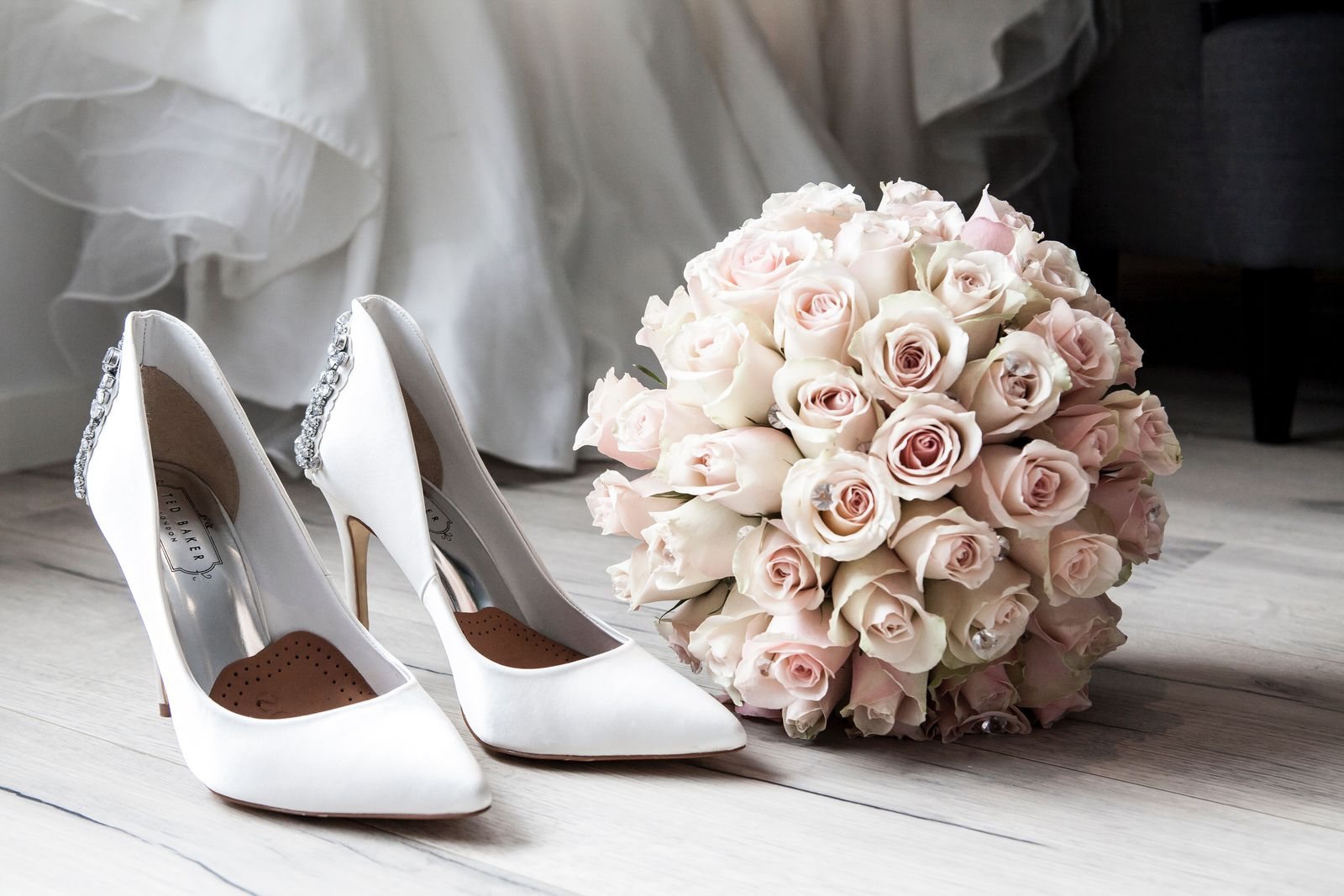 Weiße Brautschuhe neben einem Strauß rosa Rosen